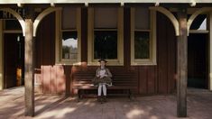 a woman is sitting on a bench in front of a building with columns and windows