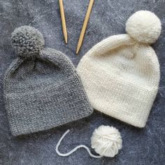 two knitted hats and knitting needles on a gray surface next to each other,