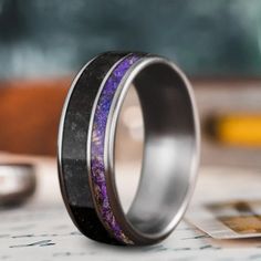 two wedding bands with purple and black inlays are sitting next to each other