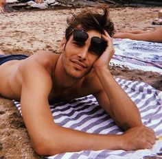 a shirtless man laying on a towel at the beach with his head in his hands