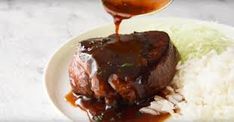 a white plate topped with meat covered in gravy and rice next to a spoon