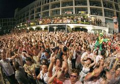 a large group of people standing in front of a building with their hands up to the sky