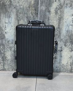 a black suitcase sitting on the ground in front of a concrete wall with no one around it