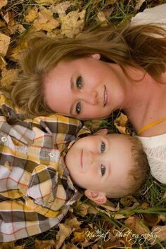 a mother and her son laying in the leaves on the ground looking at the camera