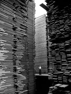 a black and white photo of a person standing in front of stacks of wooden boxes