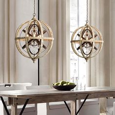 two chandeliers hanging over a table in a room with white walls and curtains