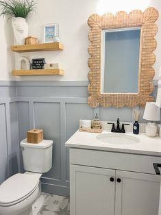 a white toilet sitting next to a sink in a bathroom under a mirror above a wooden shelf