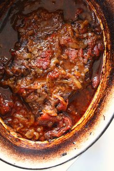 a pot filled with meat and sauce on top of a white countertop next to a wooden spoon