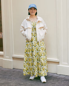 a woman standing in front of a white building wearing a blue hat and yellow dress