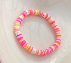 a close up of a bracelet on a white surface with pink, yellow and green beads