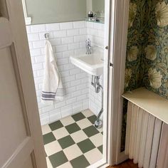 a bathroom with green and white wallpaper, tile flooring and a sink in the corner