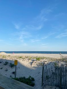 a wooden bench sitting on top of a sandy beach next to the ocean under a blue sky