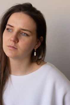 a woman with long hair and blue eyes stares into the distance while standing against a white wall