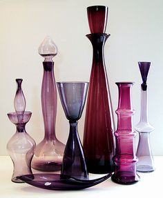 many different colored glass vases lined up on a table with white wall behind them