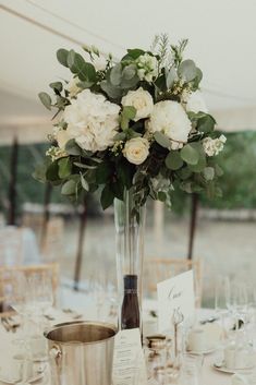 a vase filled with white flowers sitting on top of a table next to wine glasses