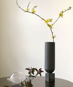 a black vase with yellow flowers in it on a table next to a white plate