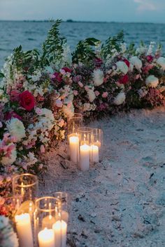 candles are lined up on the sand by the water