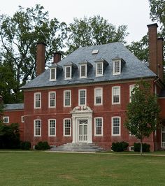 a large red brick building sitting on top of a lush green field next to trees