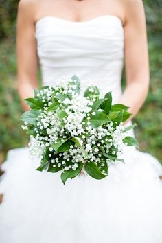 a woman in a white dress holding a bouquet of baby's breath and greenery