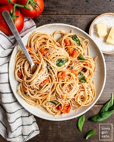 a white bowl filled with pasta and tomatoes next to sliced cheese on top of a wooden table