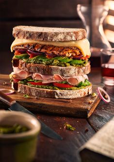 a large sandwich with meat, cheese and veggies on a wooden cutting board