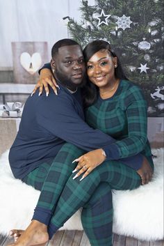 a man and woman sitting next to each other in front of a christmas tree