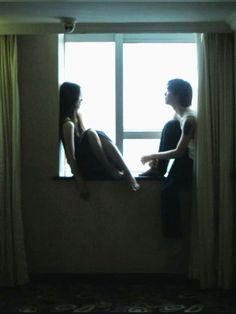 two people sitting on a window sill looking out the window