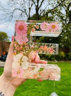 a person holding up a piece of glass with flowers on it in front of some grass