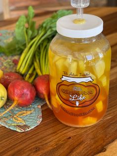 a jar filled with liquid sitting on top of a wooden table next to fruit and vegetables