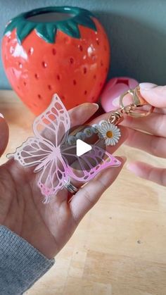 a person holding a keychain with a butterfly on it and a strawberry in the background