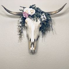 a cow skull with flowers on it's head hangs on the wall in front of a white wall