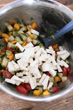 a metal bowl filled with vegetables and tofu on top of a wooden cutting board