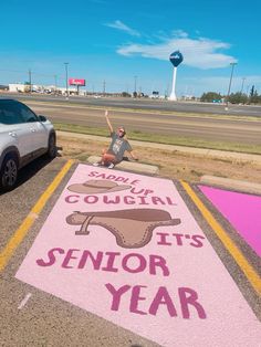 a person sitting on the ground in front of a pink sign that says senior year