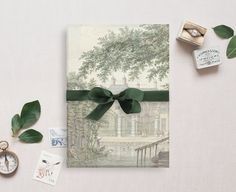 a greeting card with a green bow on it next to some stamps and a pocket watch