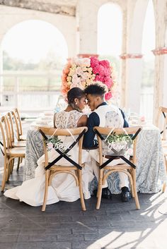 a bride and groom sitting at a table in front of flowers on the back of chairs