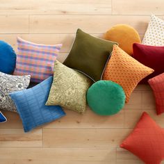 many different colored pillows laying on top of a wooden floor with one green ball in the middle