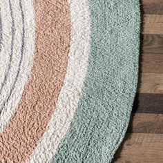 an oval rug with different colors and sizes on top of a wooden floor next to a wall