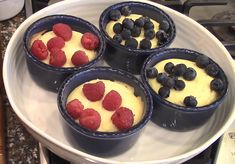 four desserts with blueberries and raspberries in them on a white plate