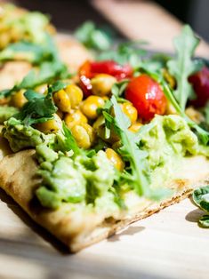 a piece of flat bread topped with veggies and other toppings on a cutting board