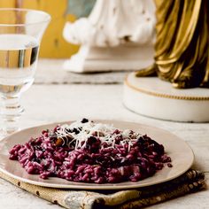 a white plate topped with red beans and cheese next to a glass of water on a table