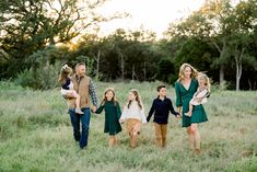 a family holding hands and walking through the grass with trees in the background at sunset