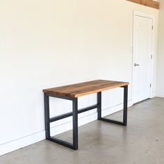 a wooden table sitting in front of a white wall with a black metal frame on it