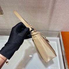 a woman's hand holding onto the handle of a beige purse with a black strap