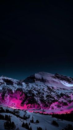 the mountains are covered in snow and lit up with pink lights at night time,