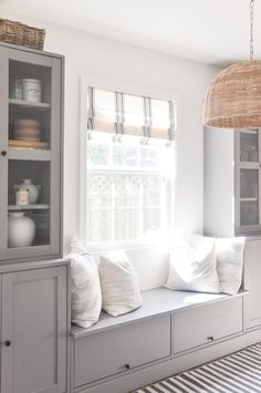 a window seat in the corner of a room next to a cabinet with pillows on it