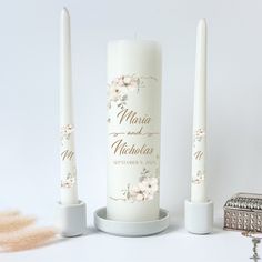 two white candles are sitting next to each other on a table with a ring box