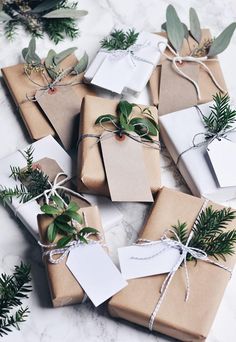 several wrapped presents tied with twine and decorated with greenery, sitting on a marble surface