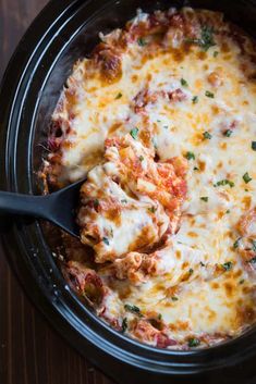 a crock pot filled with lasagna casserole on top of a wooden table