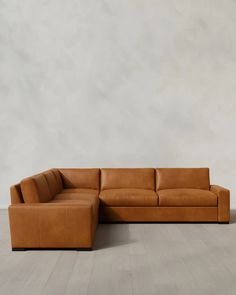 a tan leather sectional sofa sitting on top of a wooden floor next to a white wall