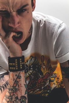 a man with tattoos and piercings on his arm holding his hand to his mouth